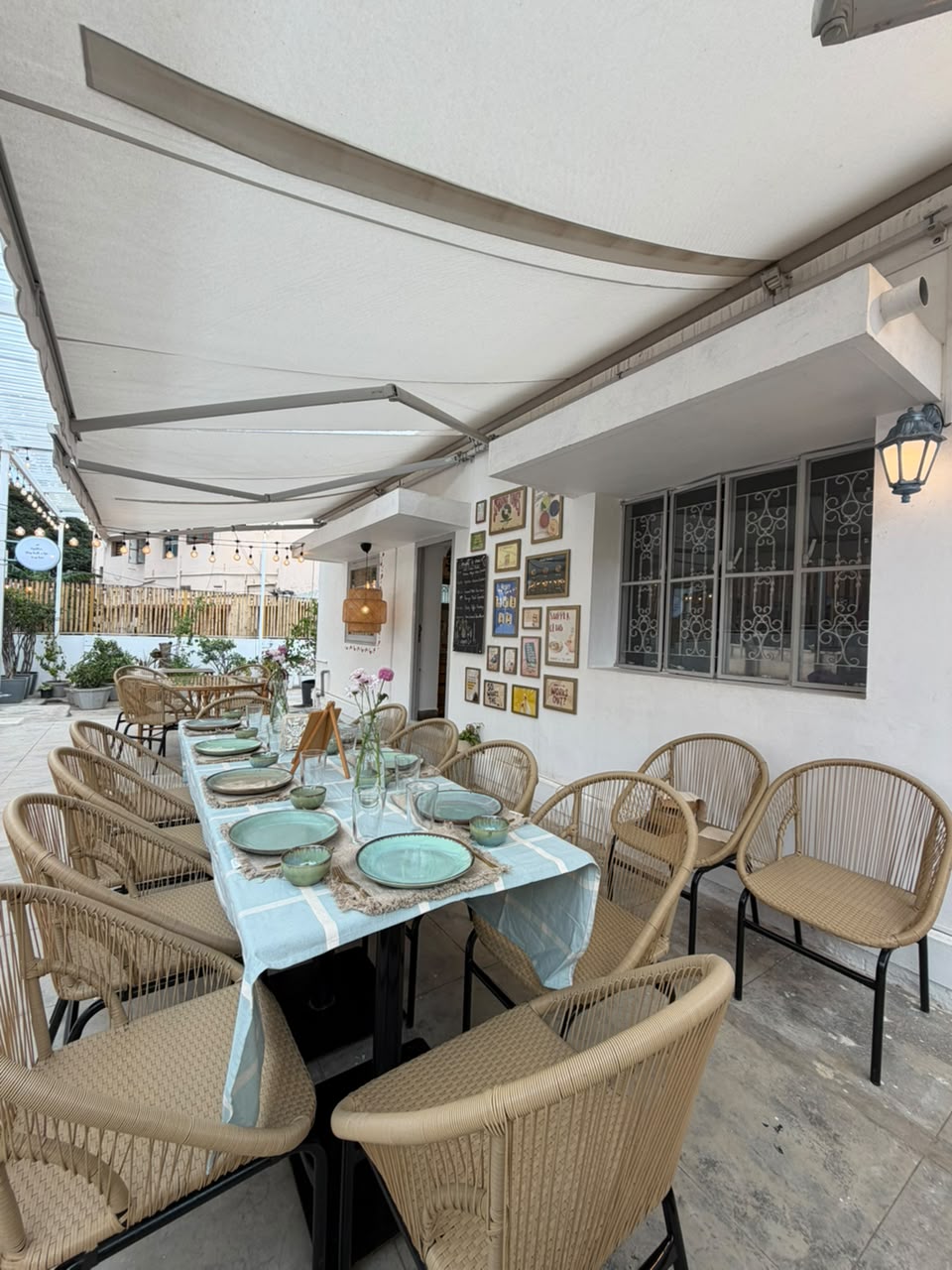 A long table set for dinner with green plates and wicker chairs on a covered terrace